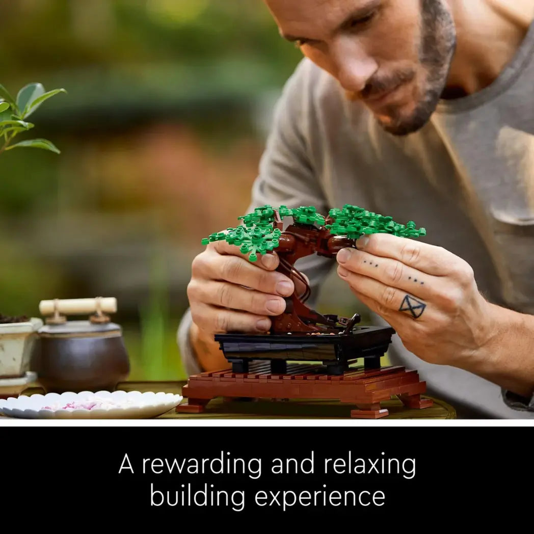 A man with hand tattoos building a LEGO Bonsai Tree with a black text banner below him saying a rewarding and relaxing building experience.