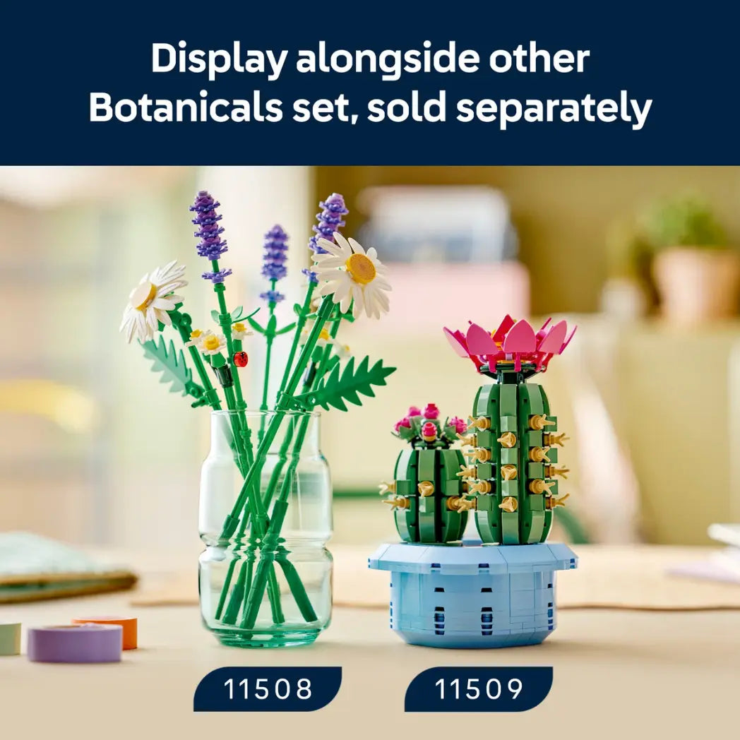 LEGO Daisies bouquet in a clear vase on a table with a lego cactus on the right and a dark blue text banner above saying display alongside other botanical sets, sold seperately.
