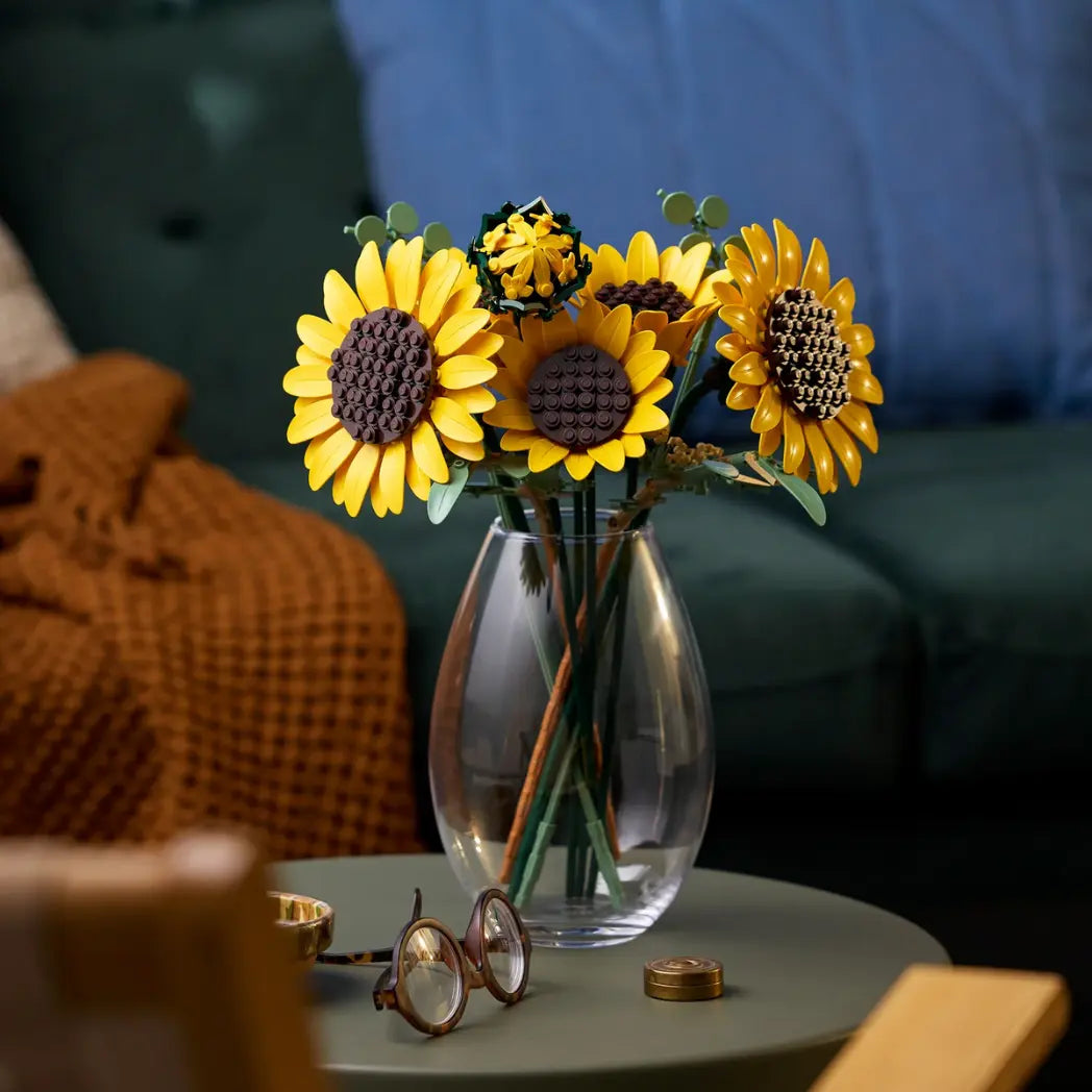 LEGO Sunflower Bouquet in a clear glass vase on a green table next to a pair of glasses.