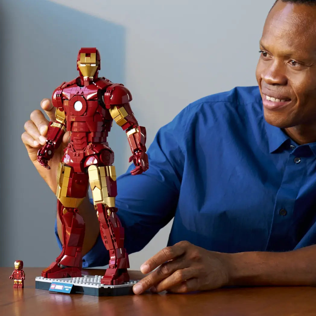 A man smiling while posing the large buildable LEGO Iron Man Mark 3 figure next to its small minifigure counterpart.