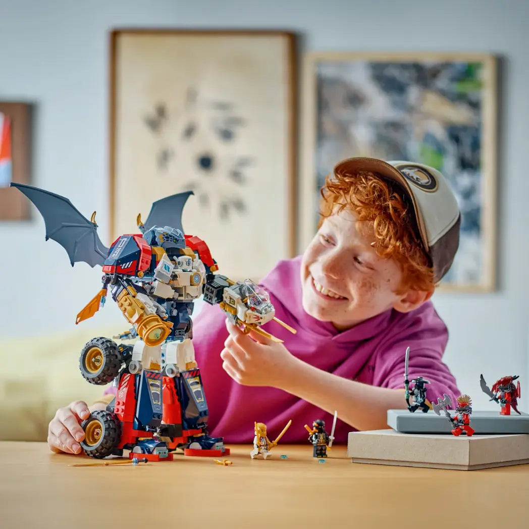 A young boy smiling while playing with the large LEGO NINJAGO Zane’s Ultra Combiner Mech on a table.