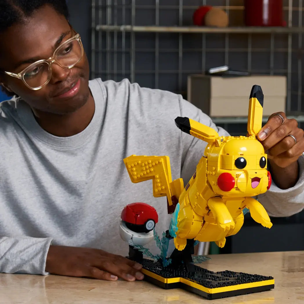 A man adjusting the ear of a buildable LEGO Pikachu figure that is posed mid-leap next to a Poké Ball.