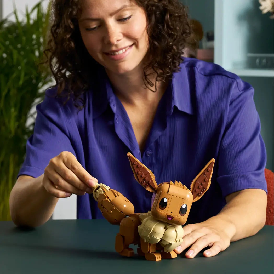 A woman smiling while posing the tail of a buildable Lego Eevee figure on a dark table.
