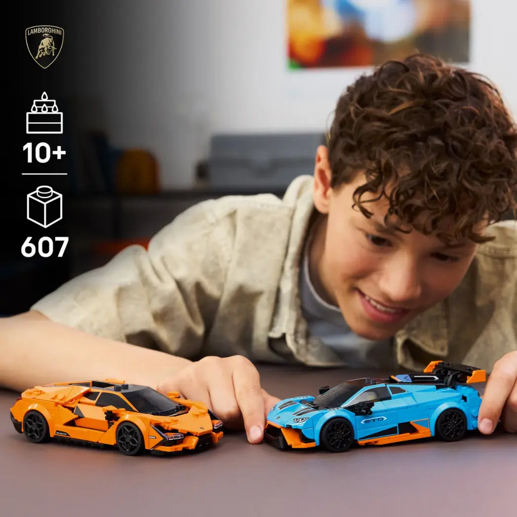 A young boy smiling while playing with an orange Lego Lamborghini Revuelto and a blue Lamborghini Huracán STO.