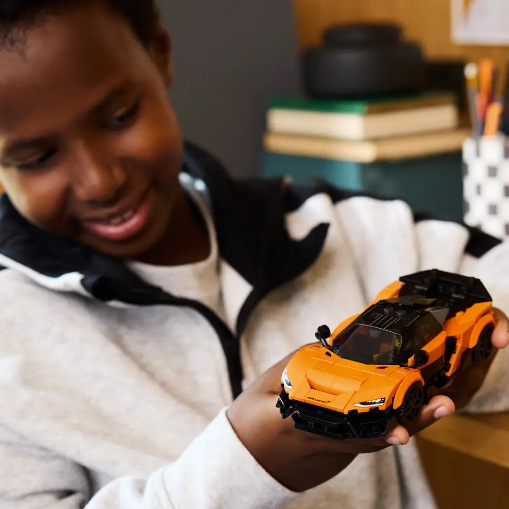 A young boy smiling while holding a completed orange and black Lego Speed Champions McLaren W1 car.