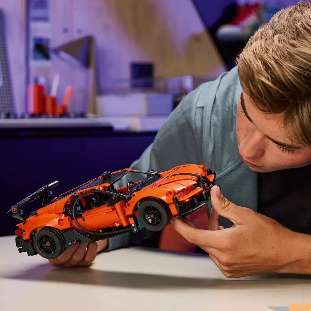 A young man looking closely at a built orange and black LEGO Technic Bugatti Chiron Pur Sport car he is holding.